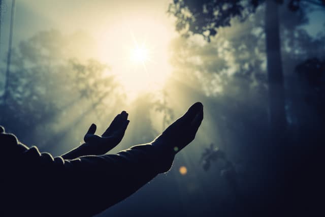 Silhouette of a figure standing on a mountain peak beneath rays of light